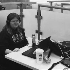 Picture of university student wearing headphones and sitting at table with computer open.